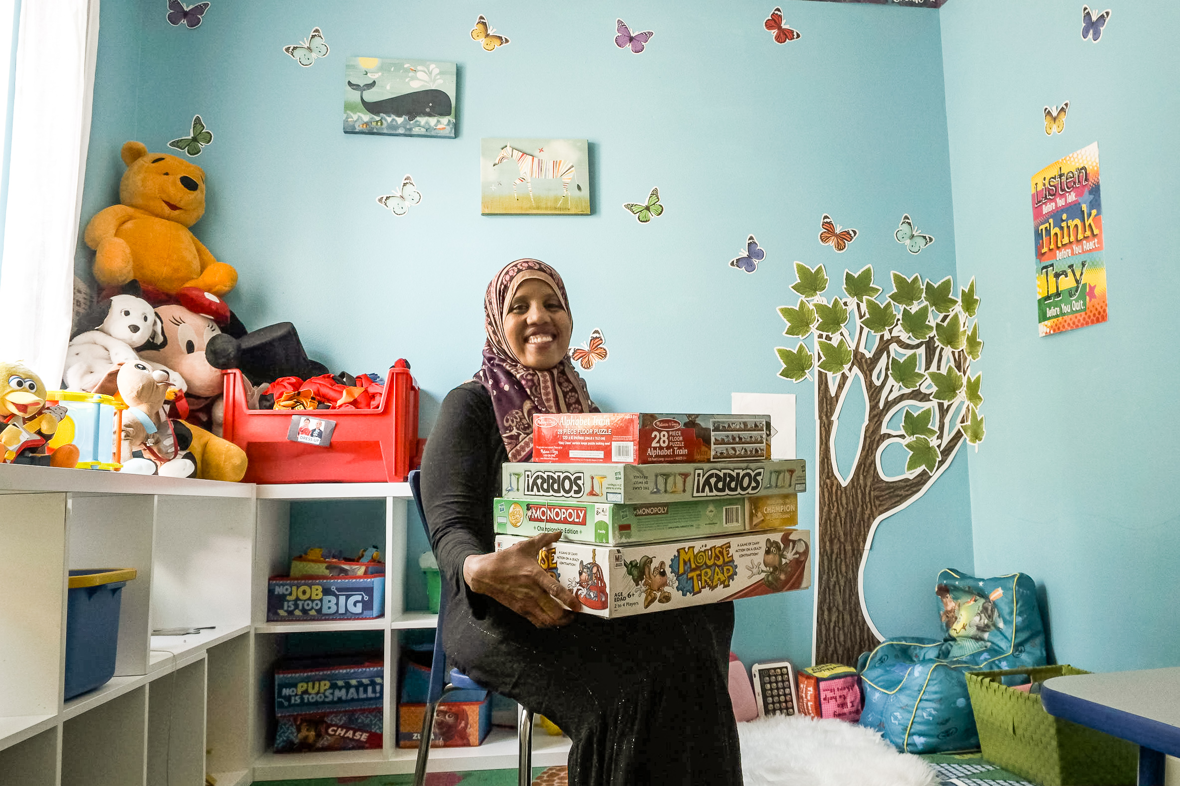 Yasmin seated and holding games in a room full toys