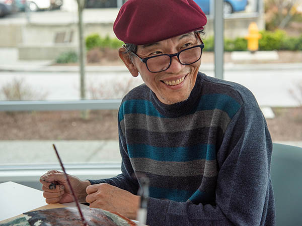 Man smiling, seated in front of his artwork