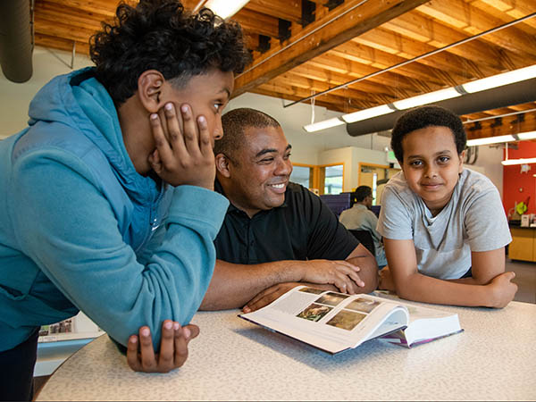 Young man and two teens chat and look at book together