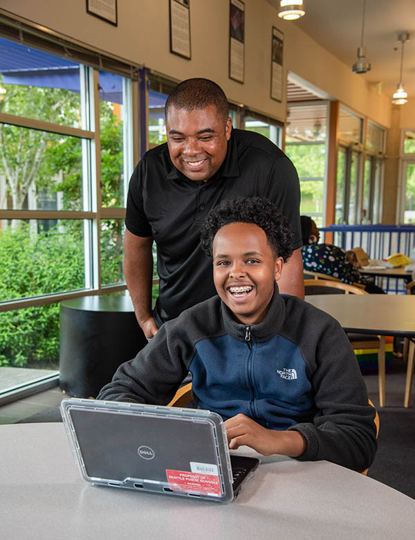 Young man assists teen boy sitting at a desk