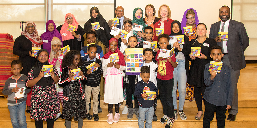 Group of adults and children holding up Somali alphabet book