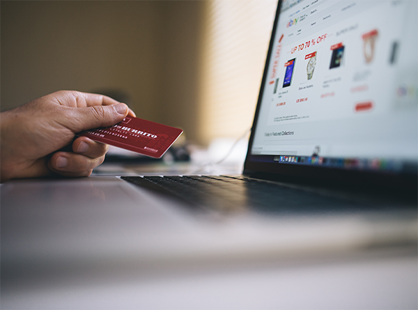 Hand holding a credit card in front of a laptop