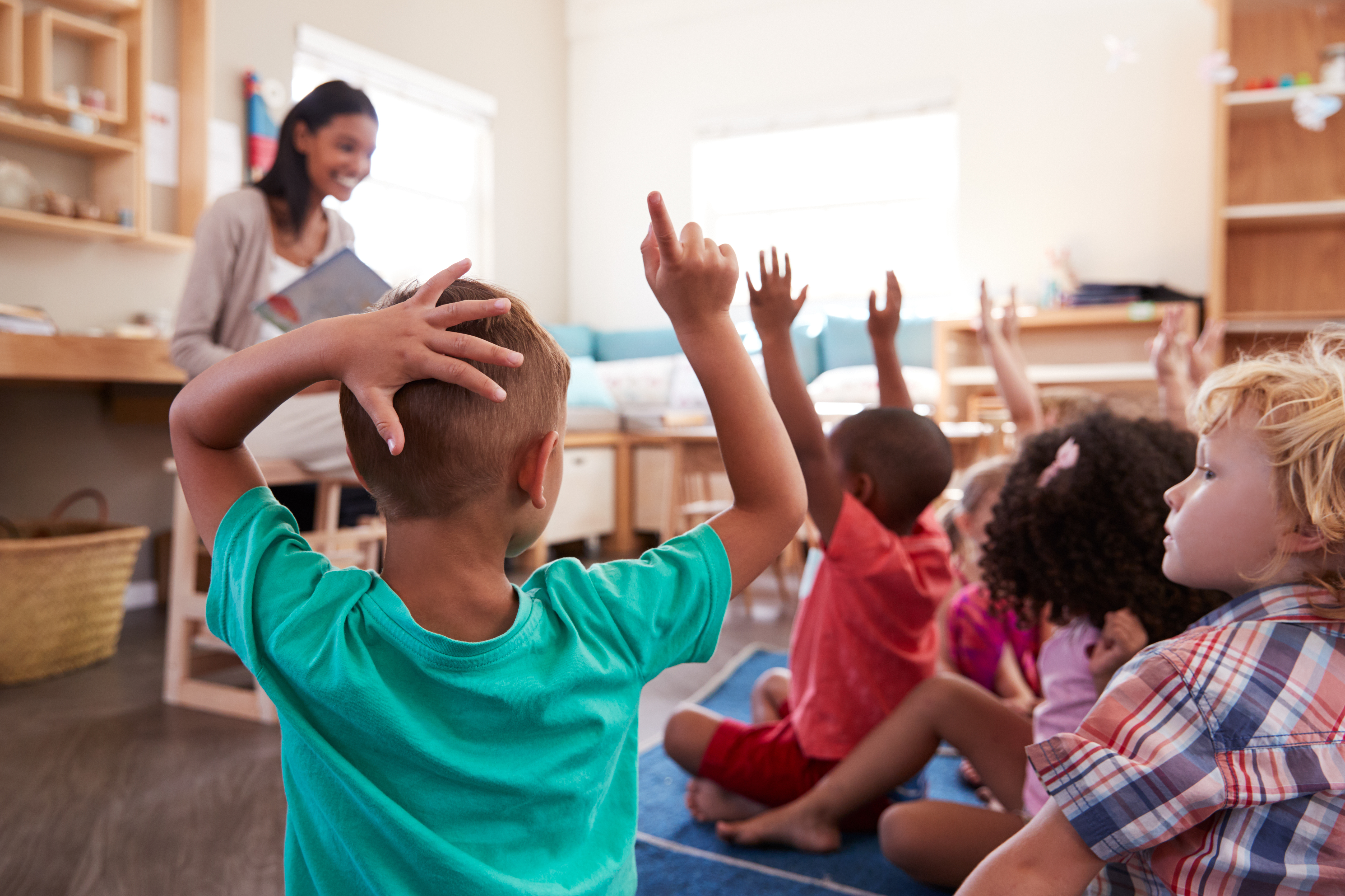 Children raising hands in classroom with teacher