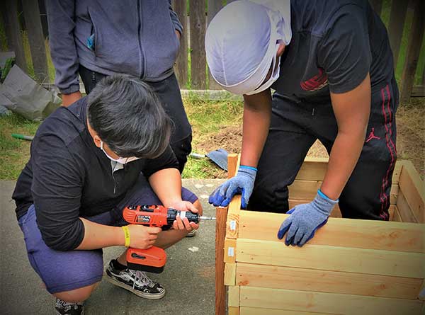 Man and teen boys build raised garden bed for NewHolly youth garden
