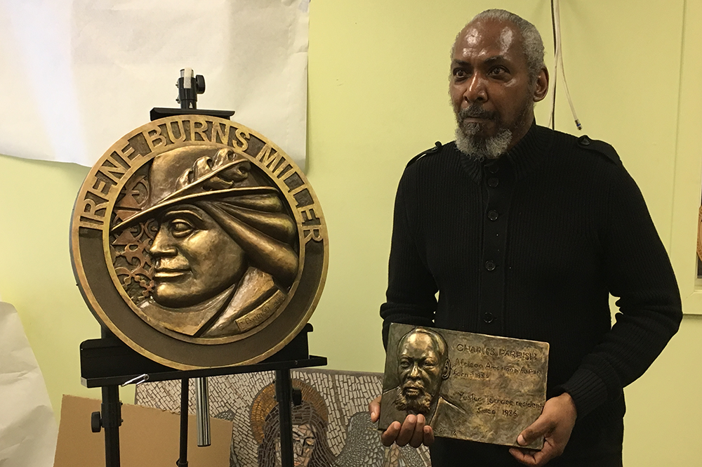 Man holding bfronze plaque standing next to bronze medallion