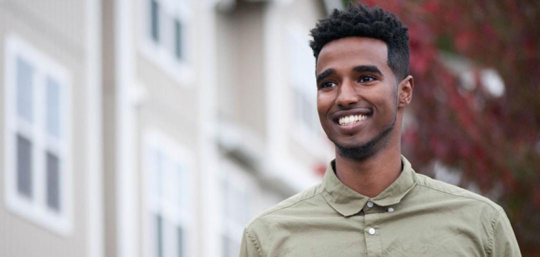 Smiling young man stands in front of a residential building