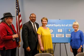 SHA Executive Director Andrew Lofton and residents standing with Senator Patty Murray with "Digital Equity Act of 2019" panel behind them