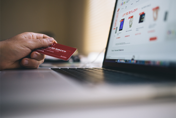 Hand holding a credit card in front of a laptop