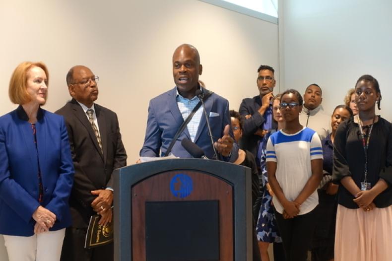 Man at podium with group of people surrounding him