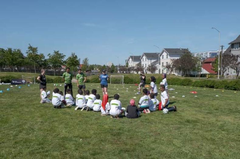 Youth seated on a soccer field listening to adult soccer players