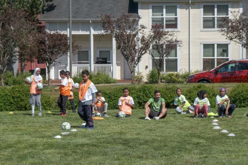 Kids seated on a field, some holding soccer balls