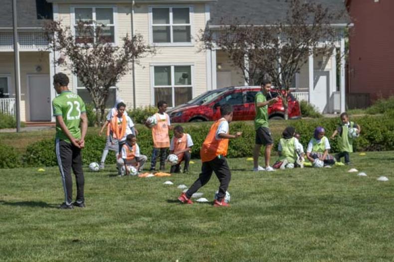Boys and girls standing on soccer field with two adult soccer players