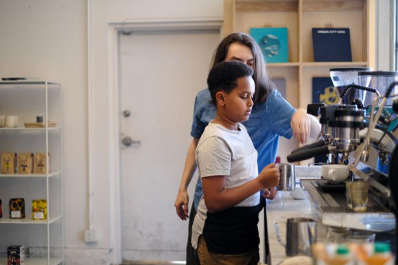 Teenage boy holds metal cup to steam milk at coffee bar