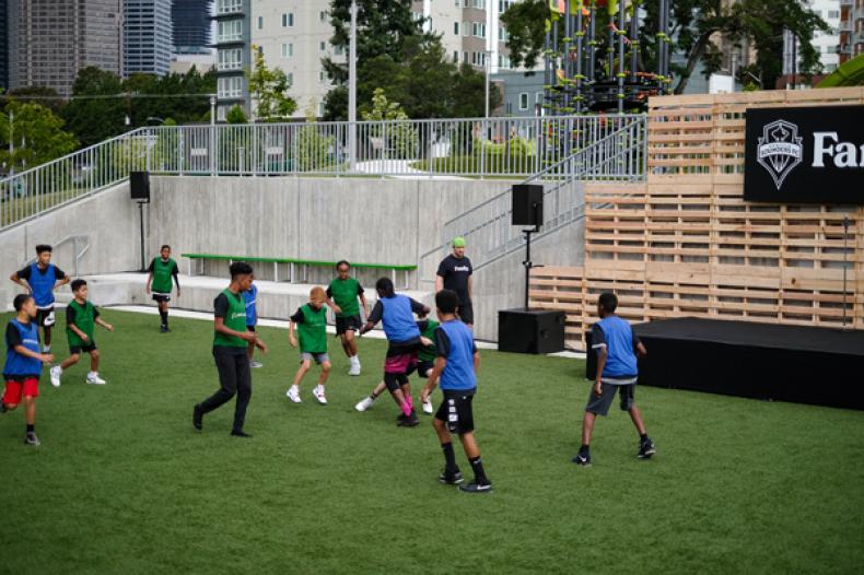 Adults and children kick ball around RAVE soccer field at Yesler Terrace Park
