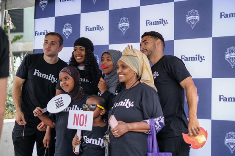 Group of players and general public standing against 'Family' backdrop at RAVE Foundation event at Yesler Terrace Park's RAVE soccer field