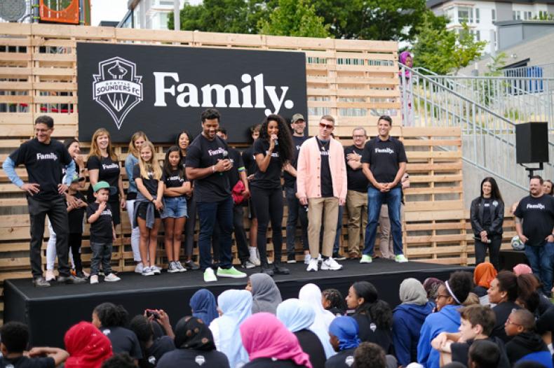 Russell Wilson, Ciara and Macklemore and others stand on outdoor stage at Rave Foundation event at Yesler Terrace Park