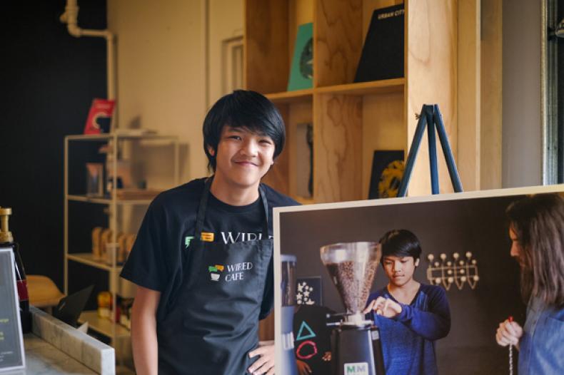 Young man stand next to panel with picture of him grinding coffee beans