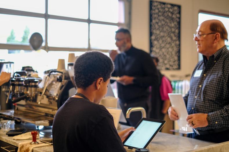 Youth looks at tablet as people give orders at coffee bar