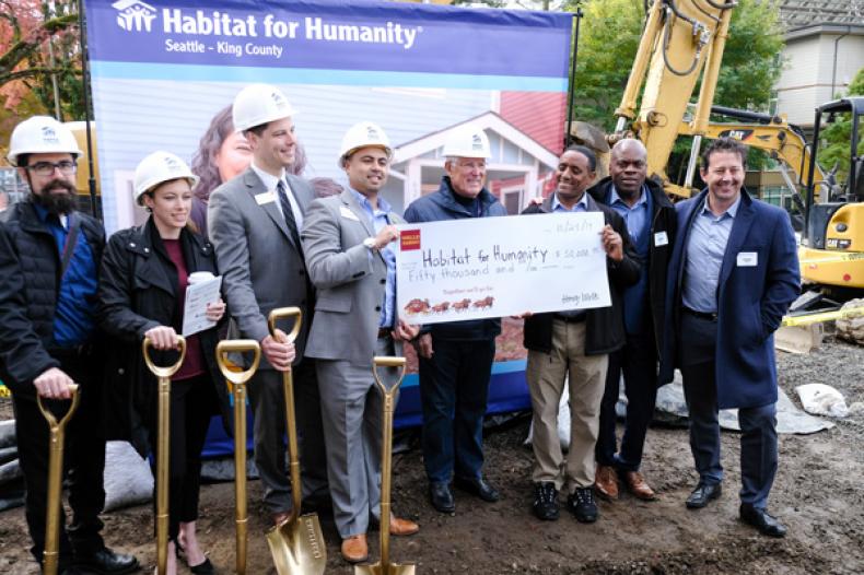 Officials hold up facsimile of check in front of "Habitat for Humanity" banner