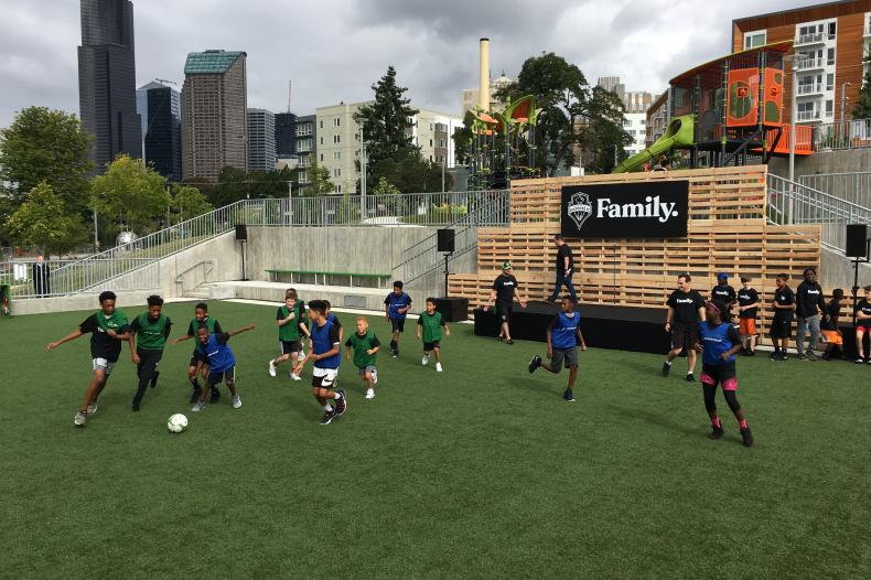 Adults and kids run around soccer field