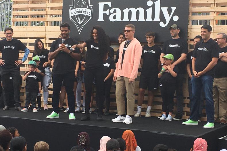 Group of adults and kids stand on outdoor stage 