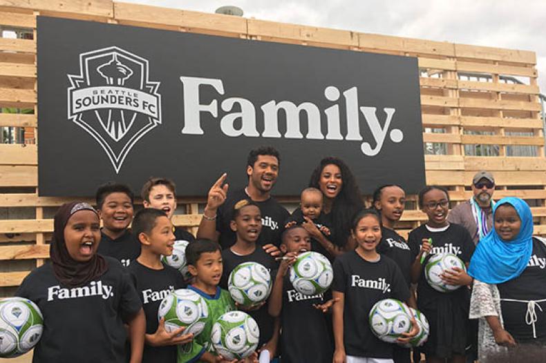 Group of adults and children standing on stage with soccer balls 