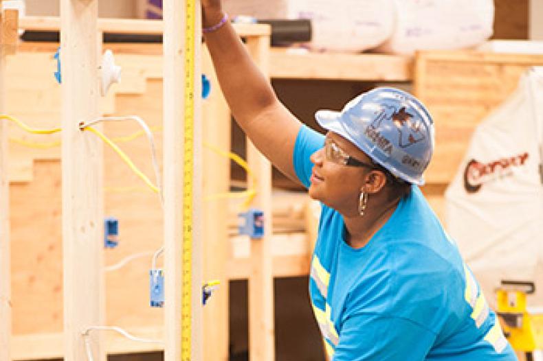 A woman in construction gear measures items at a worksite