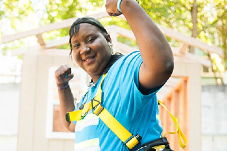 A woman in construction gear raises arms in triumphant gesture
