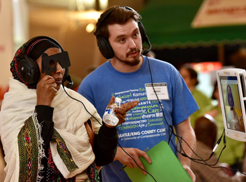 A woman reading letters on a chart for an eye test as a man stands nearby