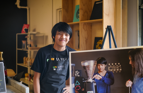 Teen boy at cafe next to panel describing youth coffee brewing program