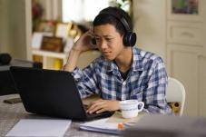Young man looking at laptop with coffee cup at his side
