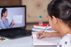 Girl sitting in fron of laptop taking notes in a notebook