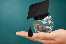 Image of hand holding a plastic piggy bank with a graduation cap on