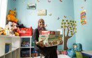 Smiling woman holds boxes of games in room filled with toys