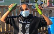 Teen wearing face covering holds up cucumbers from NewHolly youth garden