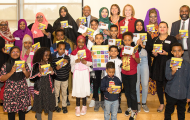 Group of adults and children holding up Somali alphabet book