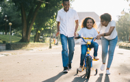 Girl learning to ride bike with two adults assisting