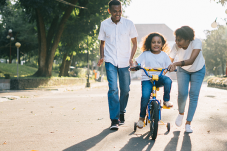 Girl learning to ride bike with two adults assisting