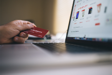 Hand holding a credit card in front of a laptop