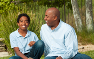 Smiling teenager and adult man sitting on the grass