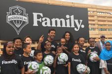 Adults and kids gather on outdoor stage with soccer balls