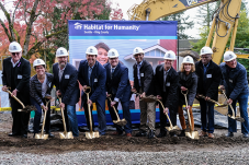 Group of people with shovels participate in groundbreaking ceremony with "Habitat for Humanity" banner in background