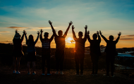 Group of youth raising arms in air at sunset