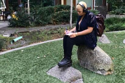 Young woman sitting on a rock while writing in notebook
