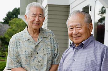 Two smiling older men stand together outside a home