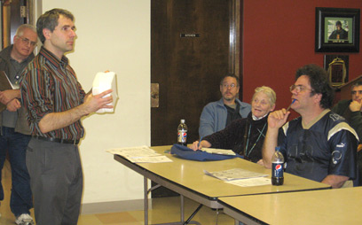 Resident community liaison Sven Koehler shows a group of Denny Terrace residents how mattress covers can protect against bedbug infestations. Standing to the left is Denny Terrace resident manager Paul Marsh and seated from left to right are Mark Moore, Judith Frank, Gregory Bruce and Cameron Hart.
